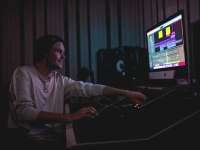 En elev mixar en låt i en studio och leer mot datorskärmen.