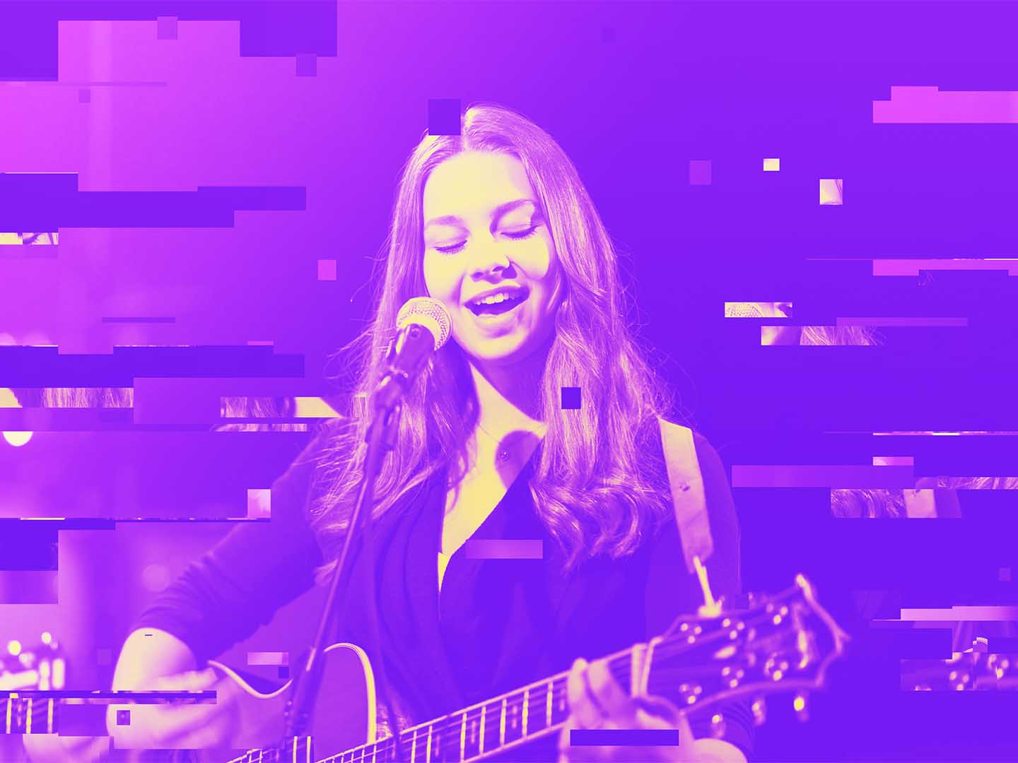 En elev sjunger i en mikrofon på en scen medan hon spelar akustisk gitarr.