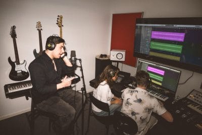 En kille sjunger medan två klasskompisar lyssnar i hörlurar vid mixerbordet.