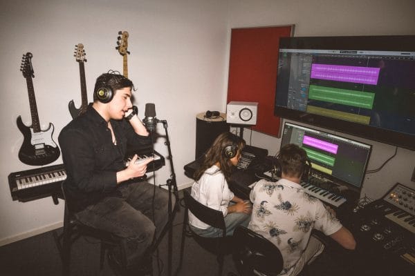 En kille sjunger medan två klasskompisar lyssnar i hörlurar vid mixerbordet.