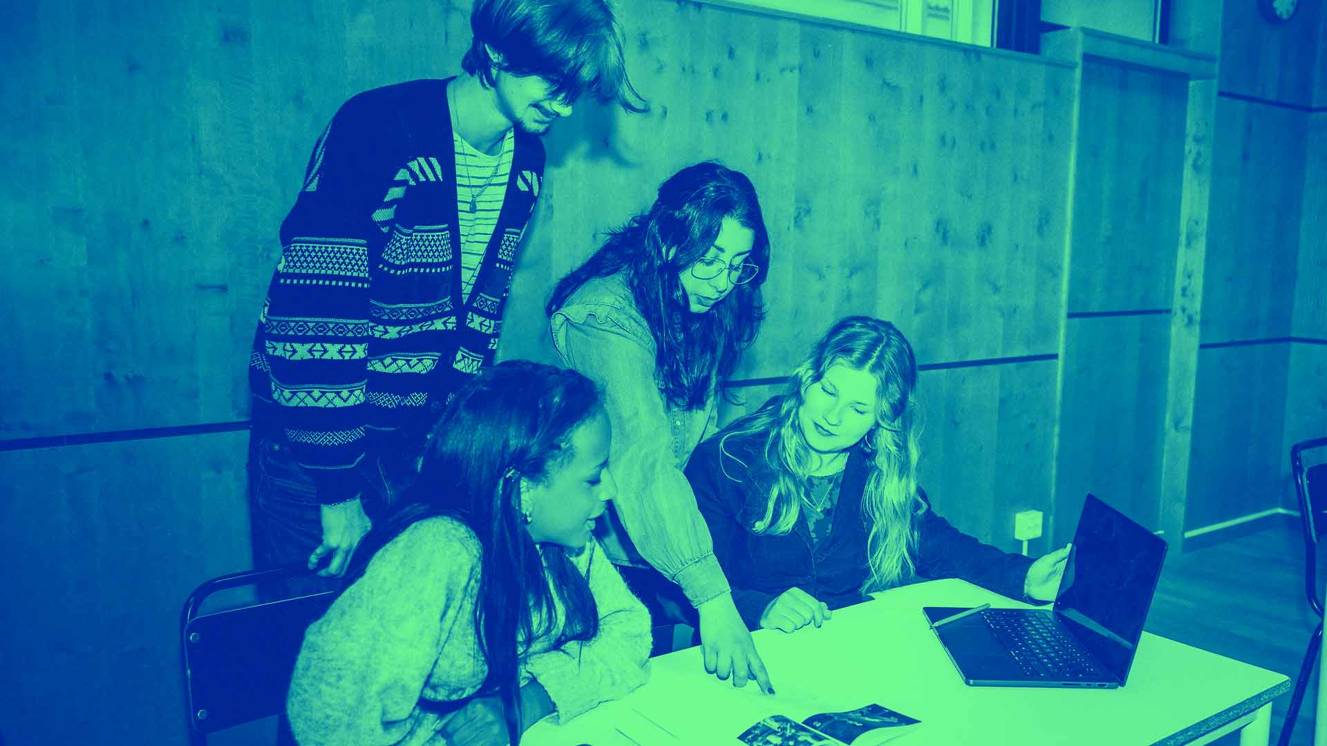 Flera elever och en lärare diskuterar ett arbete i klassrummet
